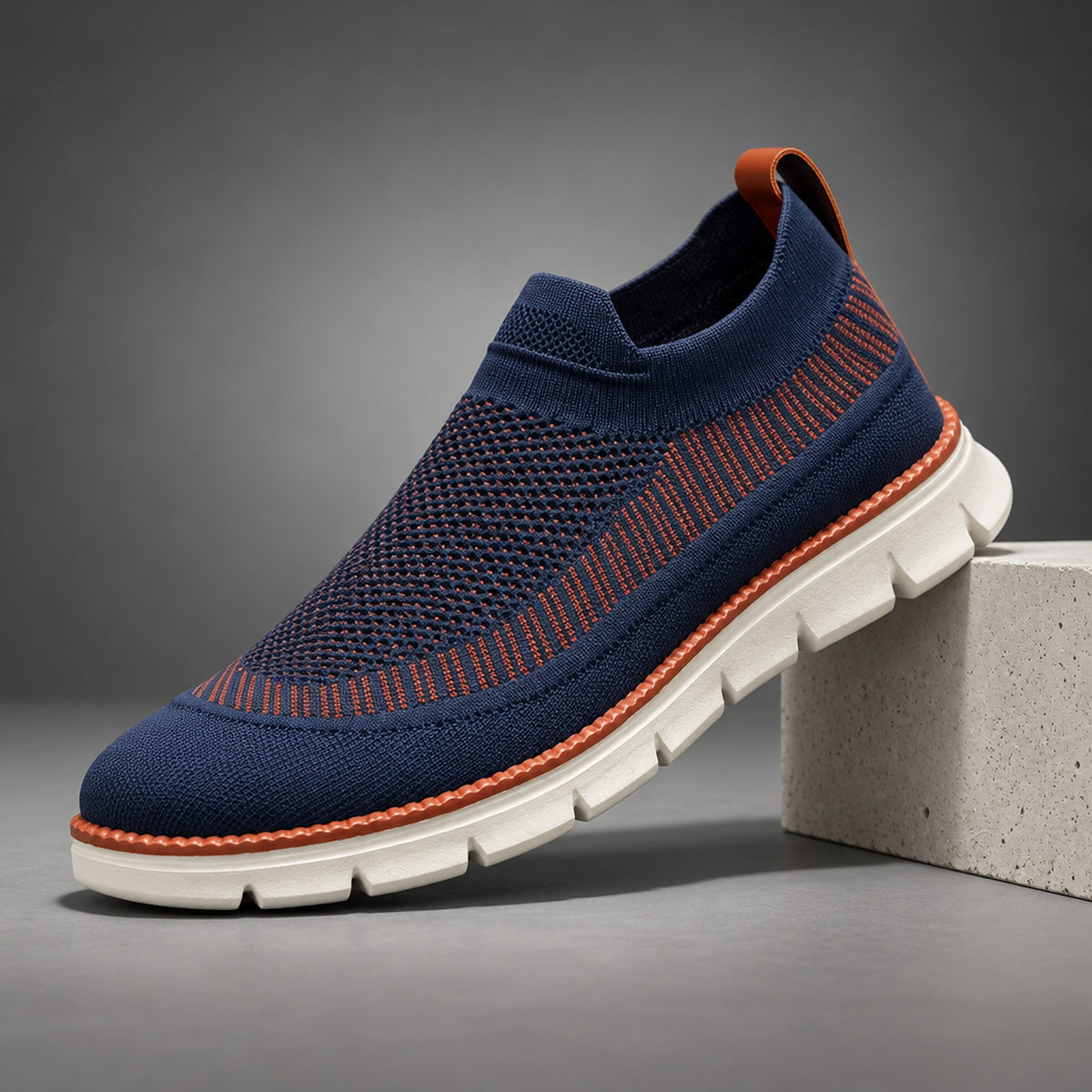 A navy blue slip-on sneaker with orange accents and stitching and an off-white sole.