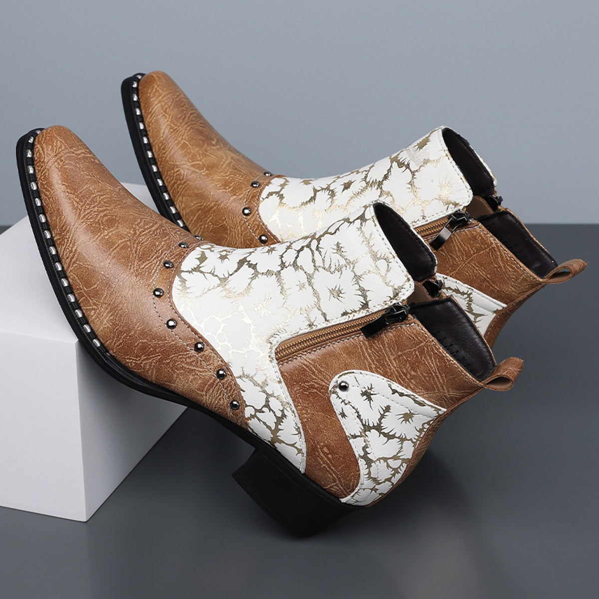 Medium brown ankle boots with cracked leather, off-white panels, gold pattern, and metal studs.